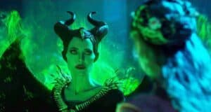 Maleficent, with her iconic horns and glowing green wings, locks eyes with a guest, surrounded by dramatic green flames.