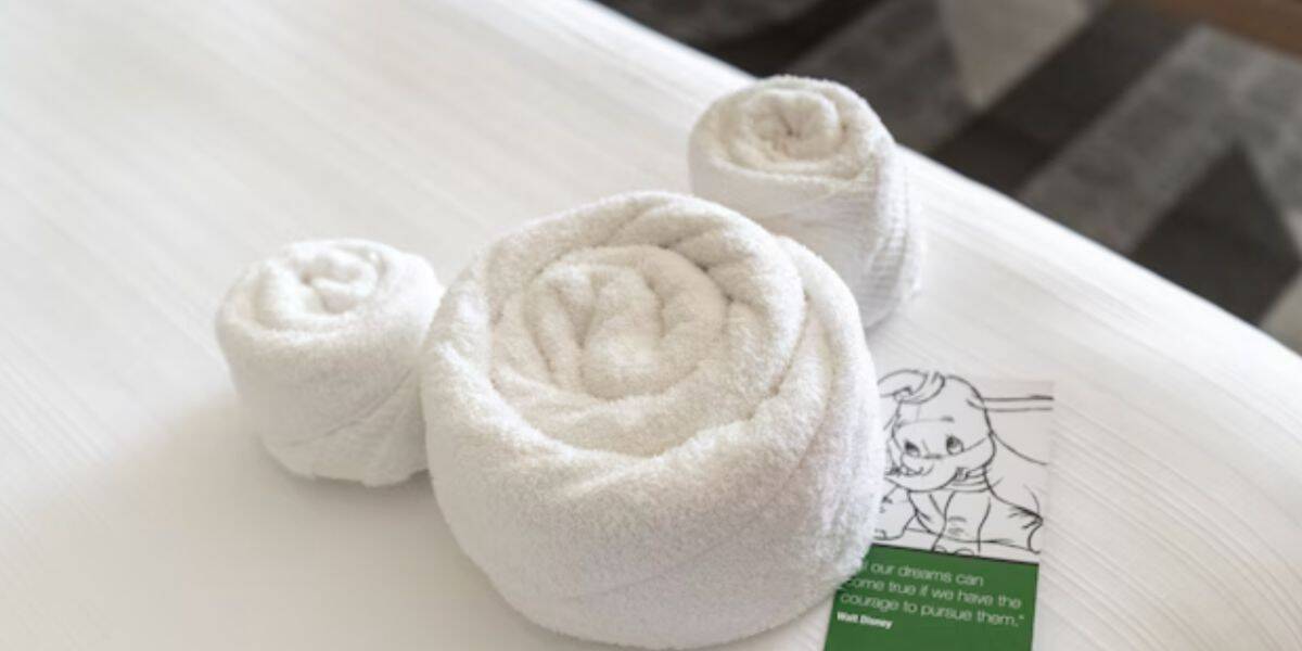 Three white towels shaped like Mickey Mouse sit on a Disney World bed, with a Mousekeeping card—a magical, nostalgic detail.