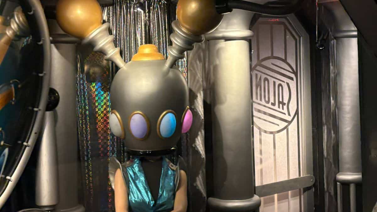 A Tomorrowland DJ icon in a striking robot helmet with antennas electrifies a gleaming, high-tech entertainment arena.