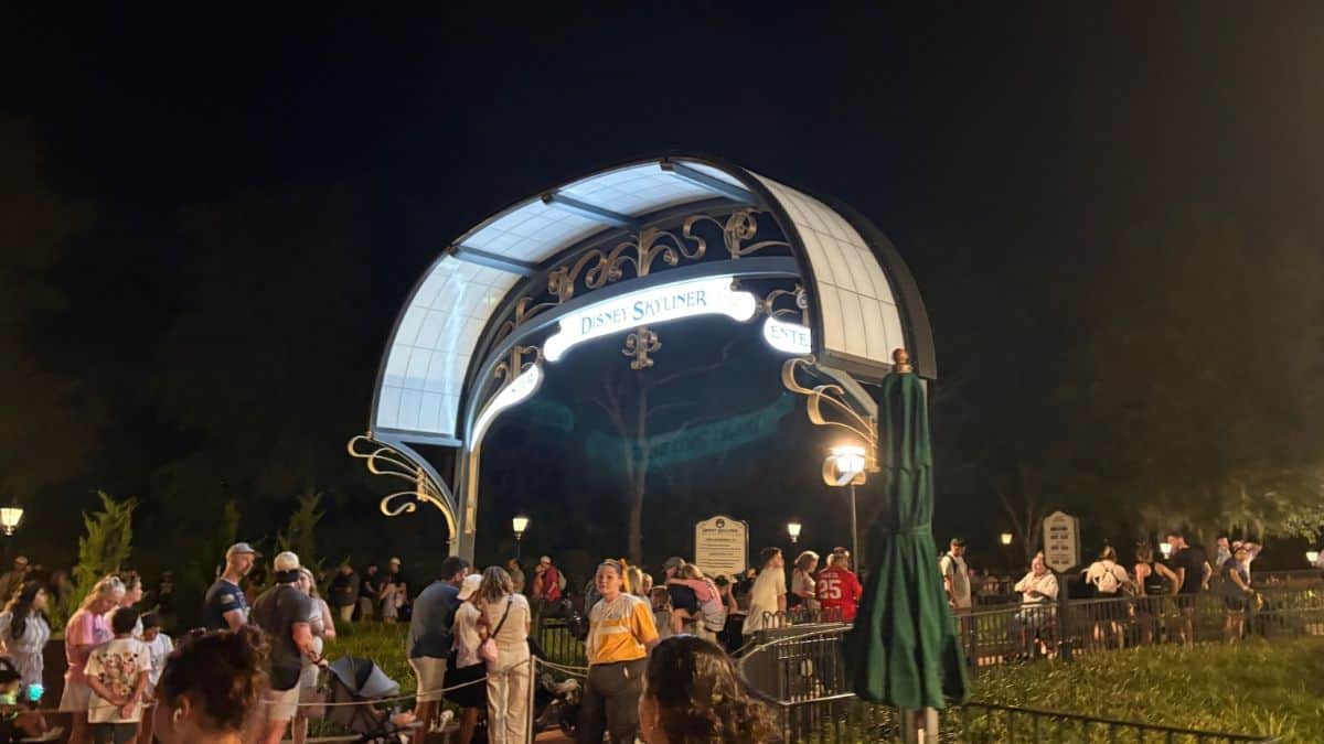 Guests line up beneath the glowing Disney Skyliner sign at park entrance, ready for a magical ride after a day at Disney World.