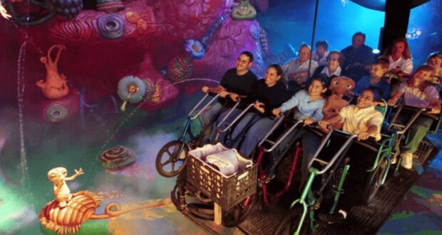 People riding a dynamic simulation ride with underwater-themed decorations including colorful coral and a character on bicycles inside of E.T. Adventure at Universal Studios Florida.