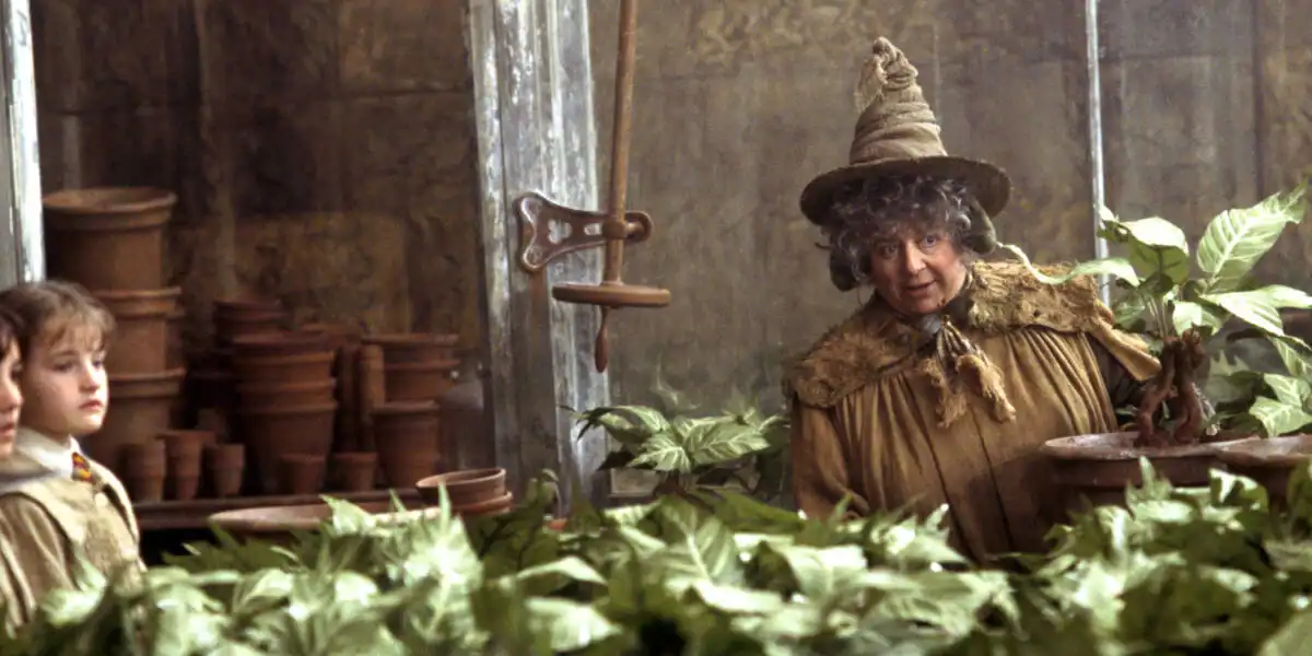 Emma Watson, in character as Hermione, explores lush greenhouse plants at the Warner Bros. Studio Tour, clay pots lining the scene.