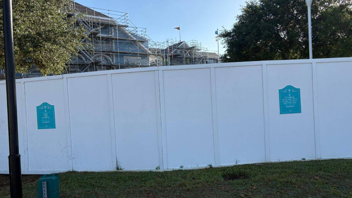 Construction fence with teal signs blocks Beach Club Resort; scaffolding and trees peek over as refurbishment continues at Disney.