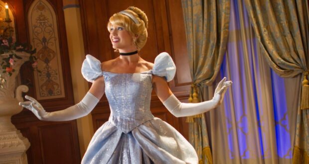 Cinderella greets guests with a smile inside Princess Fairytale Hall, set among elegant curtains and rich wood paneling.