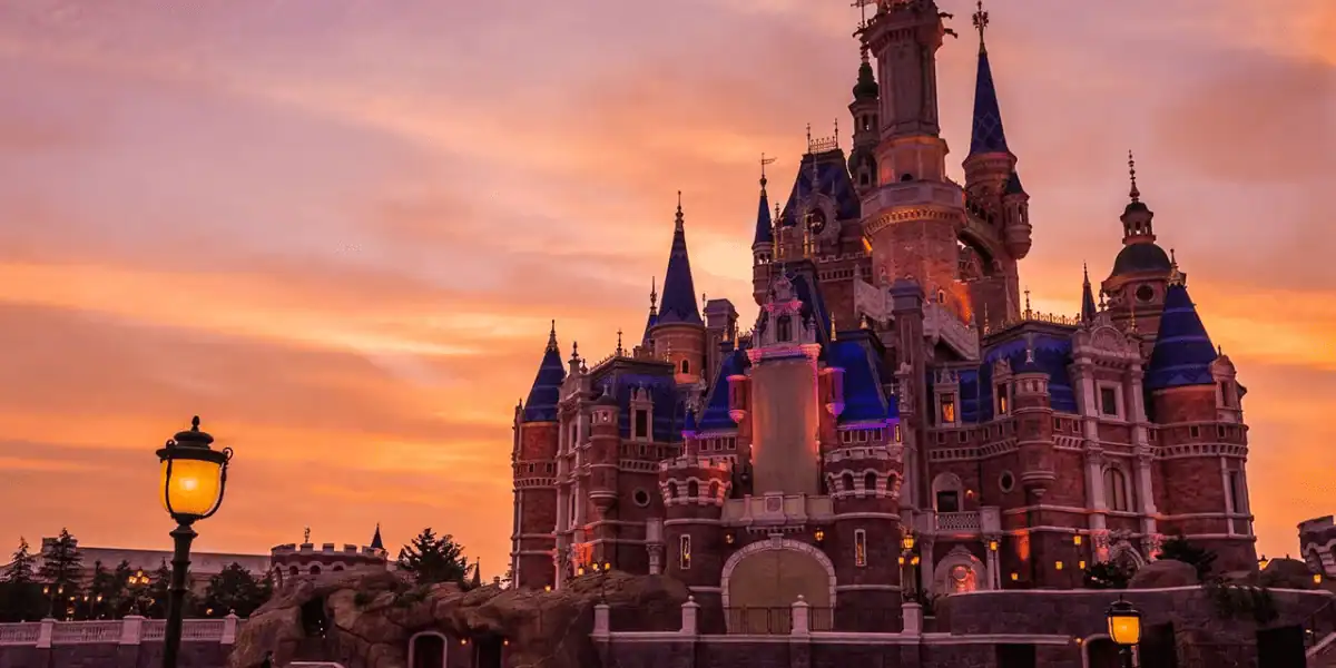 Cinderella Castle illuminated at sunset, sparkling with lights against a vivid orange sky, enchanting Magic Kingdom guests.