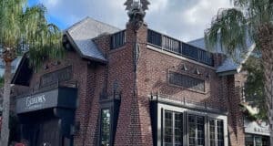 Gideon's Bakehouse at Disney World features a striking brick exterior with gothic touches and palm trees, creating an immersive villain-inspired atmosphere that draws guests into its mysterious new location.