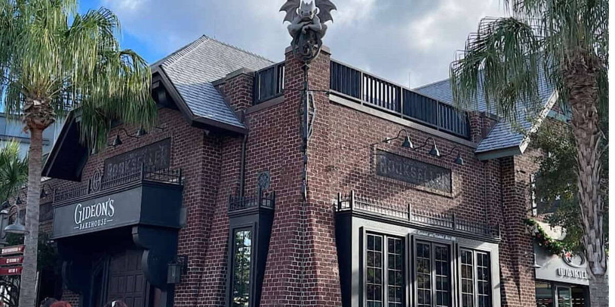 Gideon's Bakehouse at Disney World features a striking brick exterior with gothic touches and palm trees, creating an immersive villain-inspired atmosphere that draws guests into its mysterious new location.