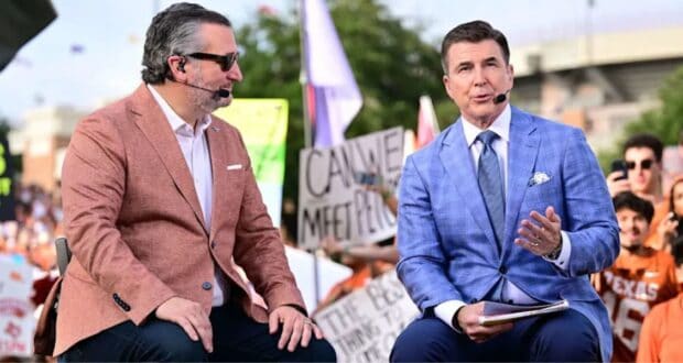 Two sports announcers in sharp suits engage in lively conversation on a broadcast stage, with an enthusiastic audience waving colorful signs and cheering wildly behind them, creating a vibrant atmosphere reminiscent of a high-energy live show you’d find at Universal Studios or ESPN Zone.