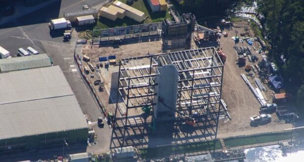 Aerial view of a new roller coaster being assembled, with twisting steel tracks taking shape and themed vehicles staged nearby for installation.