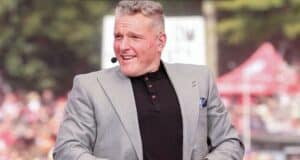 Entertainer in a sharp gray suit jacket and black shirt delivers an outdoor performance at the park, engaging the crowd with a microphone headset.