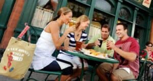 Four friends enjoying beers and food at an outdoor table at the Rose & Crown Pub in the Epcot United Kingdom pavilion.