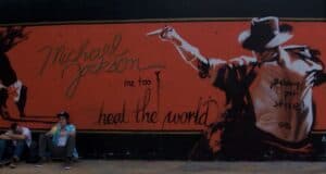 Two people sit on skateboards in front of a Universal Studios Michael Jackson mural.