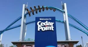 A roller coaster train crests the theme park entrance sign.