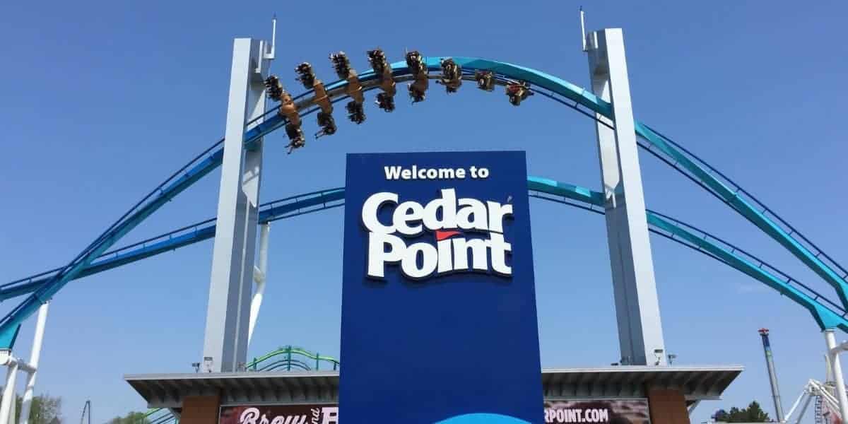 A roller coaster train cresting the blue track above the Cedar Point welcome sign.