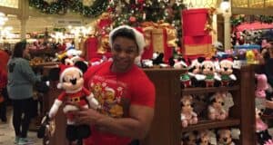 A guest wearing a Santa hat holds a Mickey Mouse plush inside the Emporium at Disney World, where Disney gift cards are accepted.