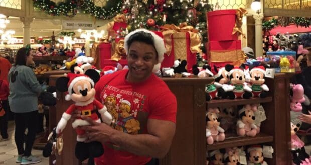 A guest wearing a Santa hat holds a Mickey Mouse plush inside the Emporium at Disney World, where Disney gift cards are accepted.