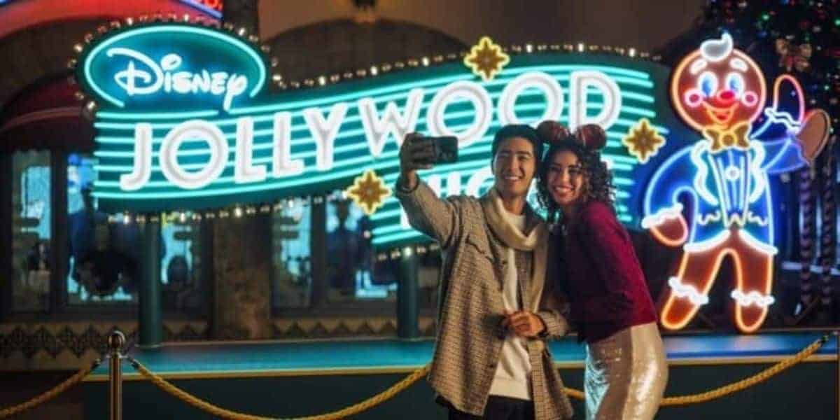Two guests taking a selfie in front of a Disney Jollywood Nights neon sign at Disney’s Hollywood Studios.