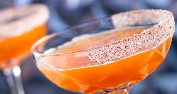 Two orange Disney holiday cocktails in coupe glasses with salt rims.
