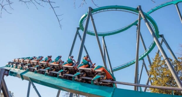 A roller coaster train climbs an inversion on the teal steel track of a thrill ride.