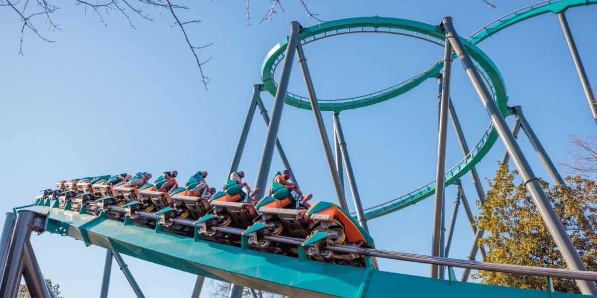 A roller coaster train climbs an inversion on the teal steel track of a thrill ride.