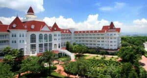 Aerial view of the Hong Kong Disneyland Hotel, featuring its signature garden maze and Victorian-style white buildings with red roofs.