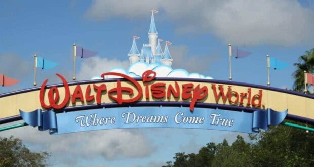 Walt Disney World entrance sign with Cinderella Castle in the background beyond the dense theme park crowds.