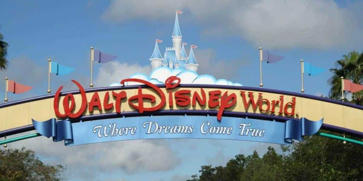 Walt Disney World entrance sign with Cinderella Castle in the background beyond the dense theme park crowds.