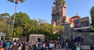 Guests gathering in front of The Twilight Zone Tower of Terror and a Monsters Inc. billboard at Disney World.