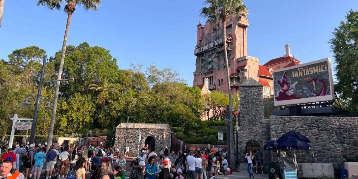 Guests gathering in front of The Twilight Zone Tower of Terror and a Monsters Inc. billboard at Disney World.