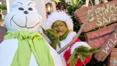 The Grinch standing next to a snowman holding a wooden sign at Universal Orlando.