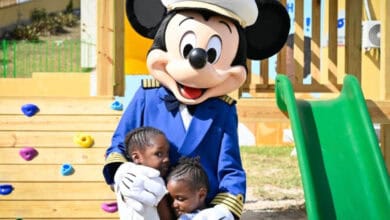 Captain Mickey Mouse hugging two children aboard a Disney Cruise Line ship.