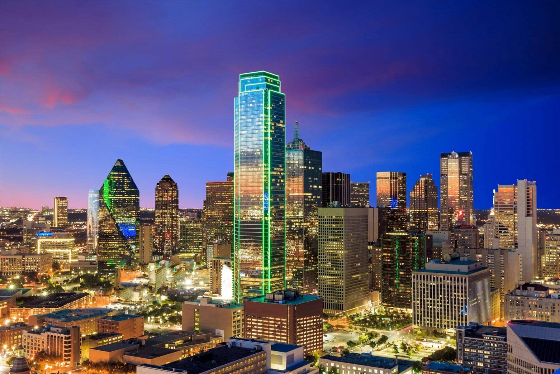 Downtown Dallas skyline illuminated at dusk with modern skyscrapers and vibrant city lights.