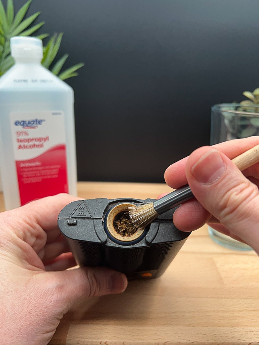 Cleaning the heating chamber of a Mighty+ vaporizer using a small brush, with isopropyl alcohol and cleaning tools in the background.