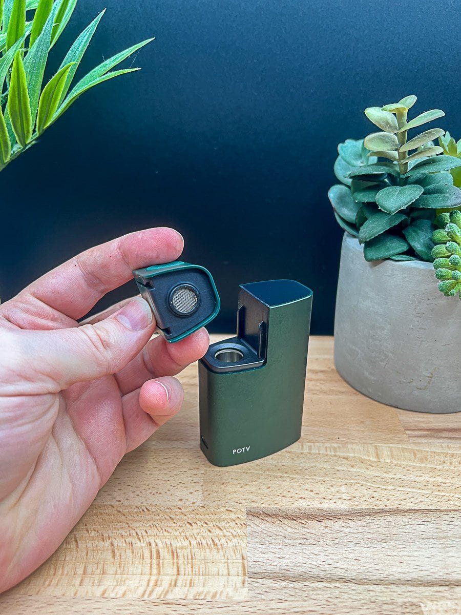 This photo features a small pile of finely ground dry herb scattered across a clean white surface, surrounded by loose pieces for a natural, organic feel. A warm wood tabletop and neutral-toned container are visible in the background, suggesting a relaxed prep environment. As covered in our POTV Lobo Review 2025, this image represents the loading process and the ritualistic, tactile side of vaporizer use.