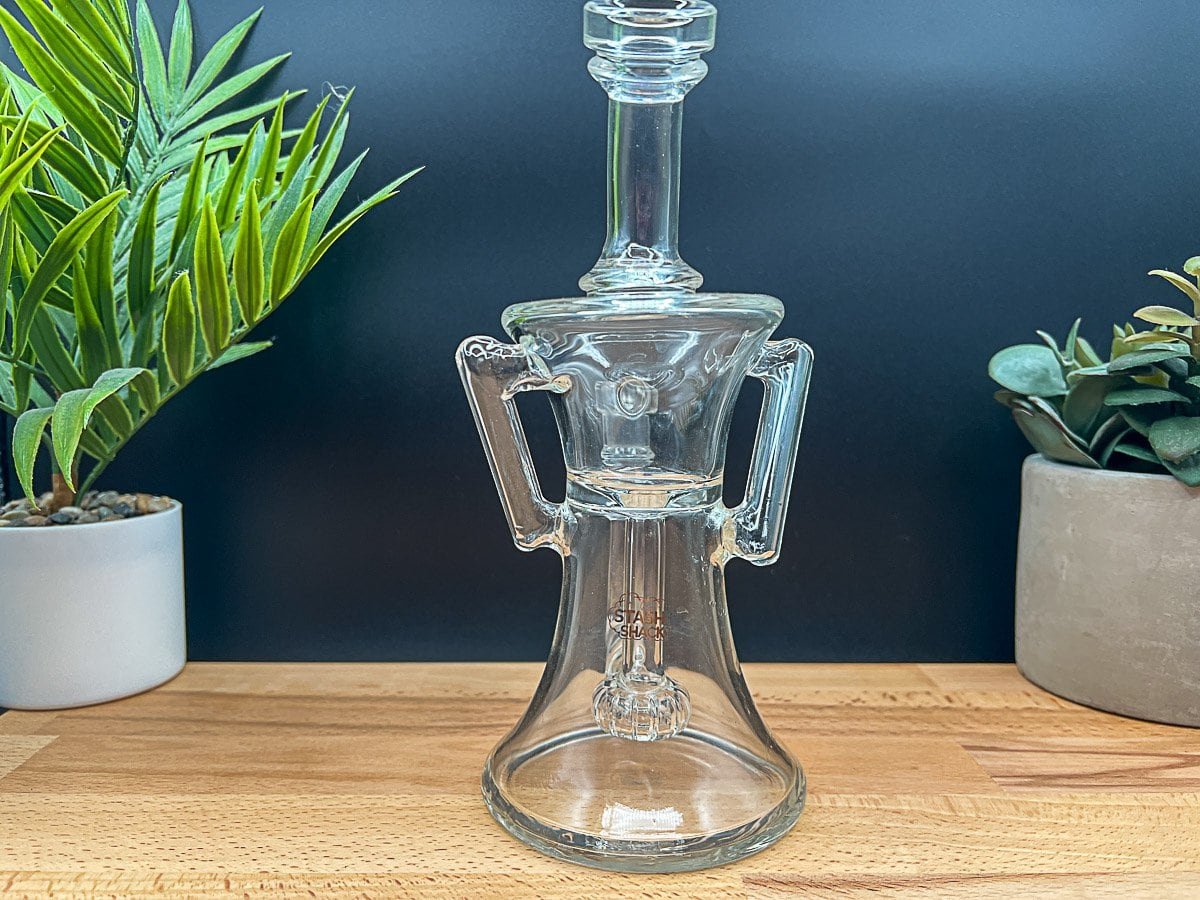 Hand holding a clear glass recycler water pipe (rig), an essential accessory for a Ruby Twist ball vape review 2025