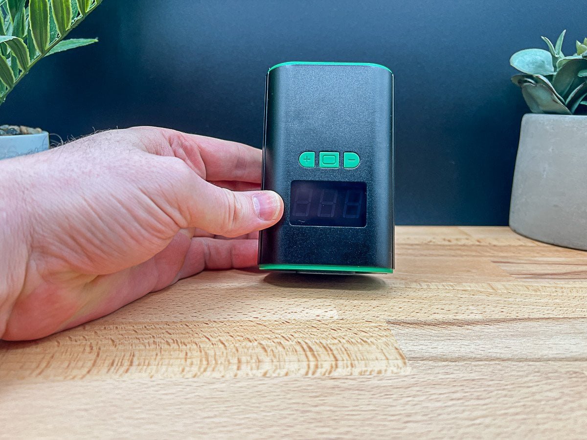 Hand adjusting a black and green PID controller with a digital display, a key component for a Ruby Twist ball vape review 2025.