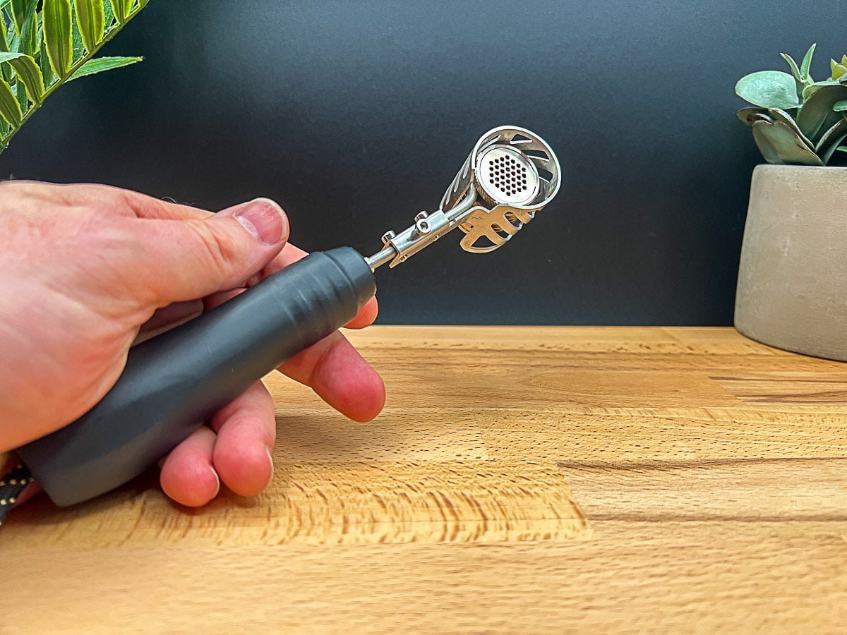 Hand holding the Ruby Twist ball vape injector head from a side angle, showing its internal screen and metal design, for a Ruby Twist review 2025.