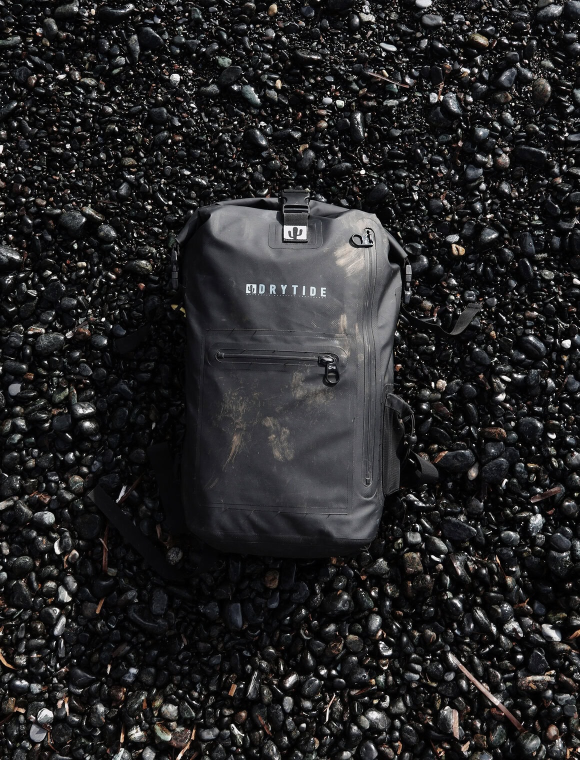 Waterproof DryTide backpack on black pebble beach surface for outdoor adventures.