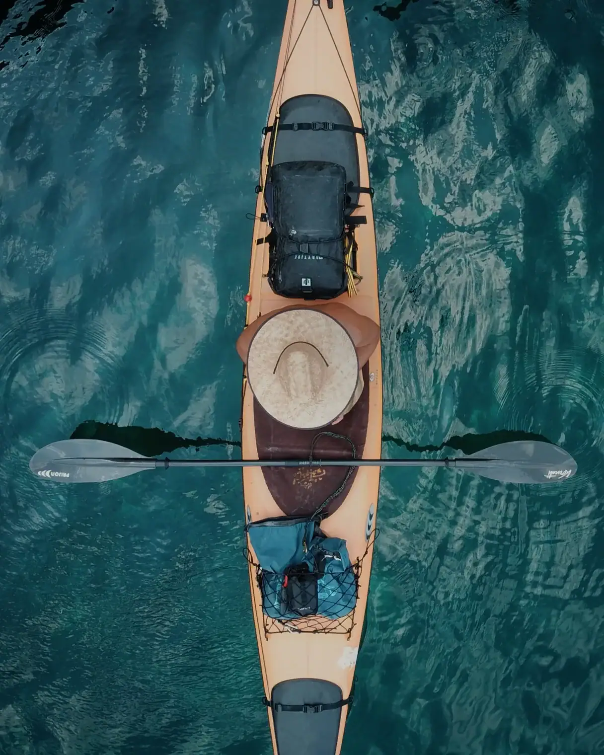 Waterproof kayak with gear and hat on water, top view.