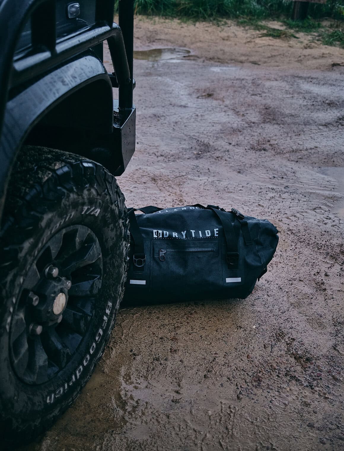 Waterproof dry bag next to off-road vehicle on muddy ground.
