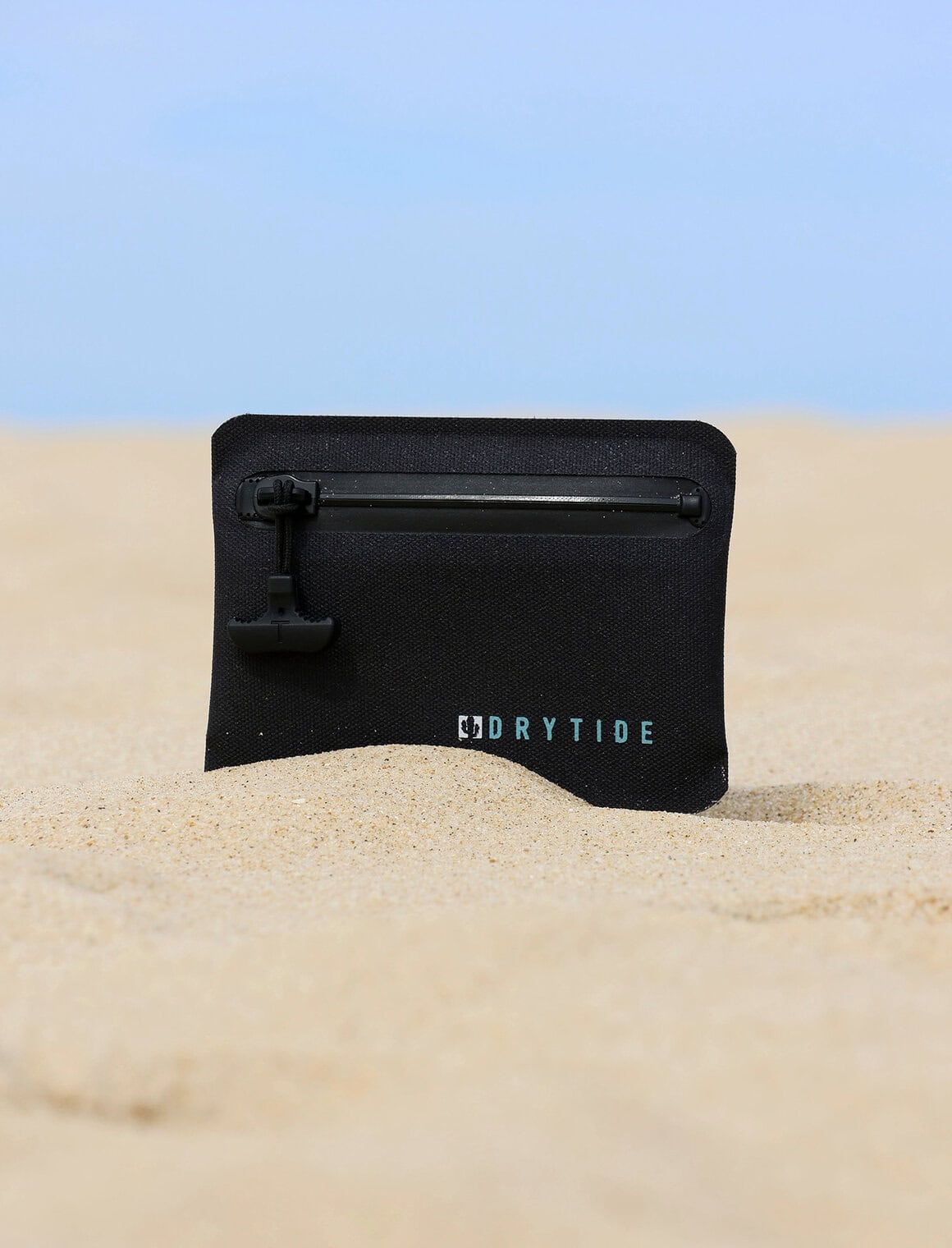 Waterproof dry bag on sandy beach with blue sky background.
