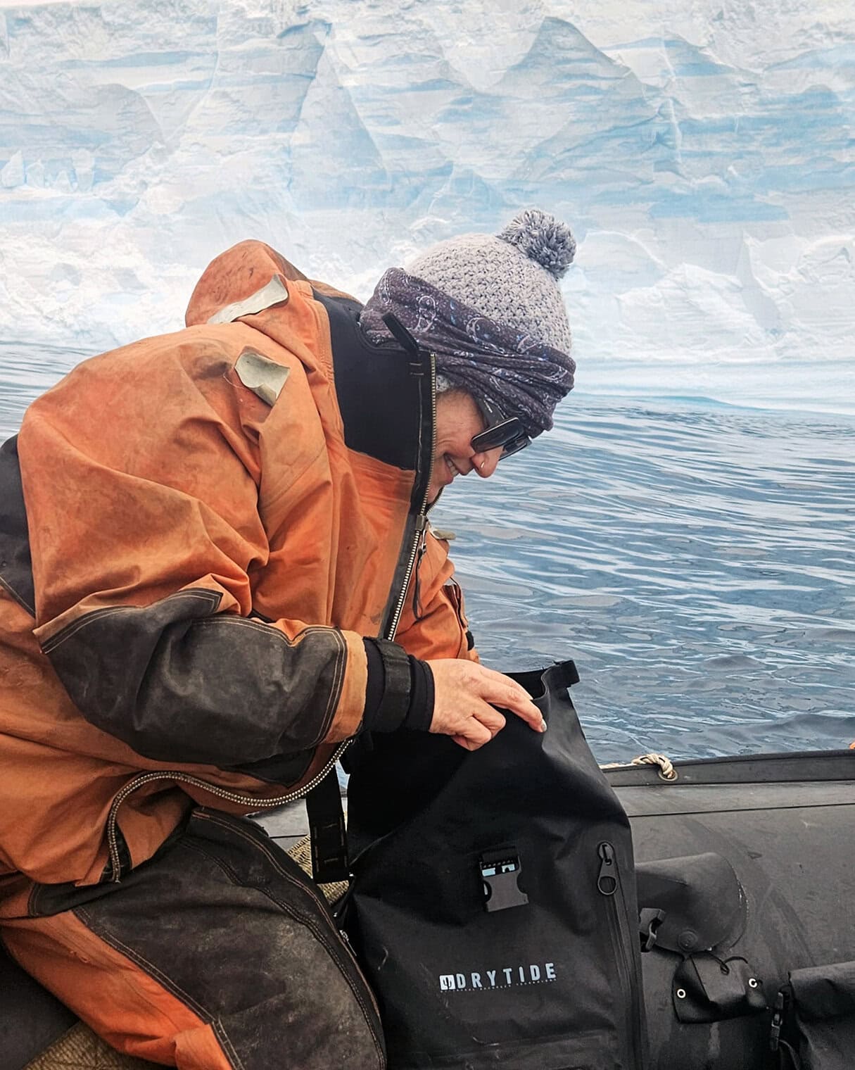 Person in waterproof gear using DRYTIDE dry bag near icy water.