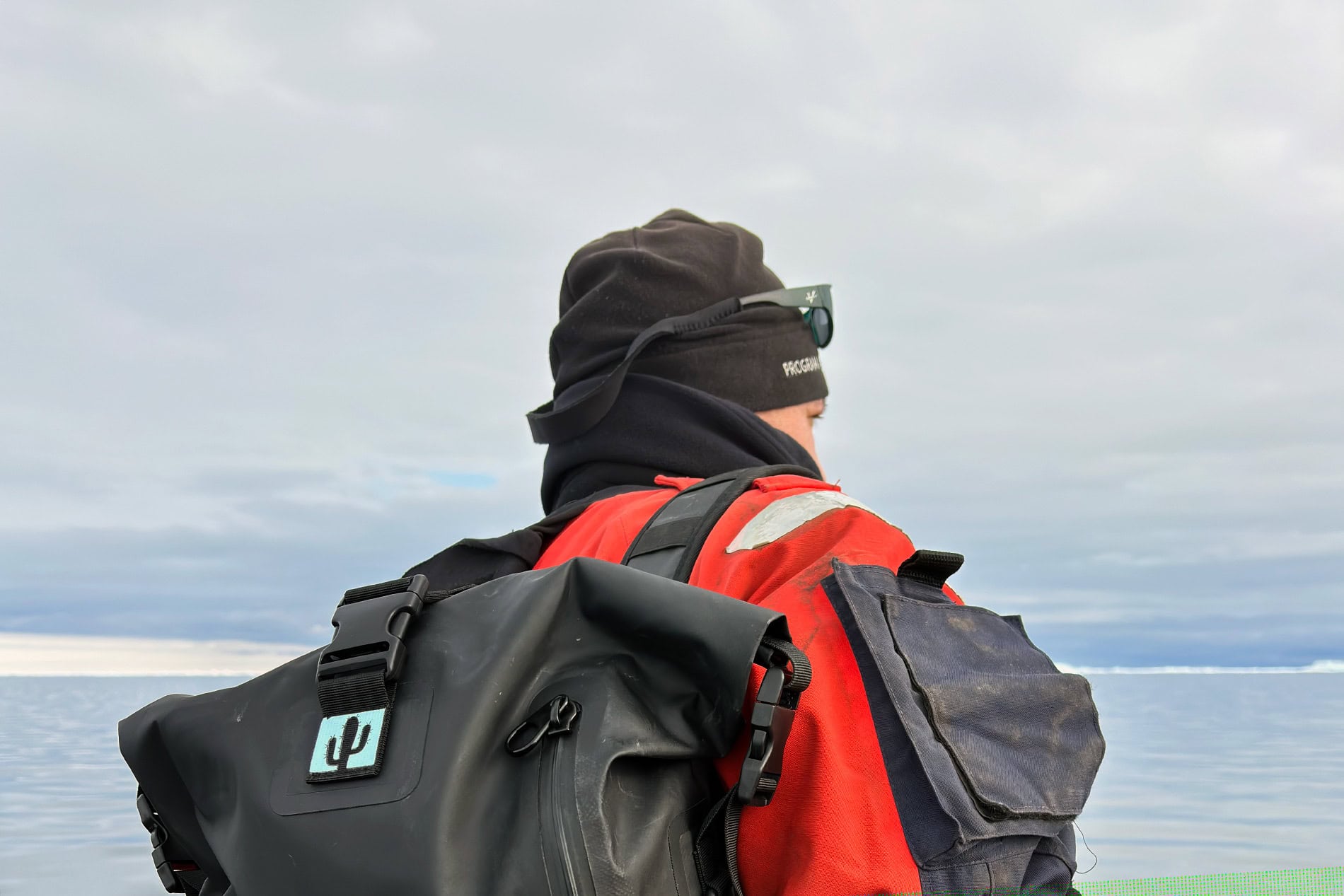 Person with waterproof backpack and duffel gear outdoors by water.