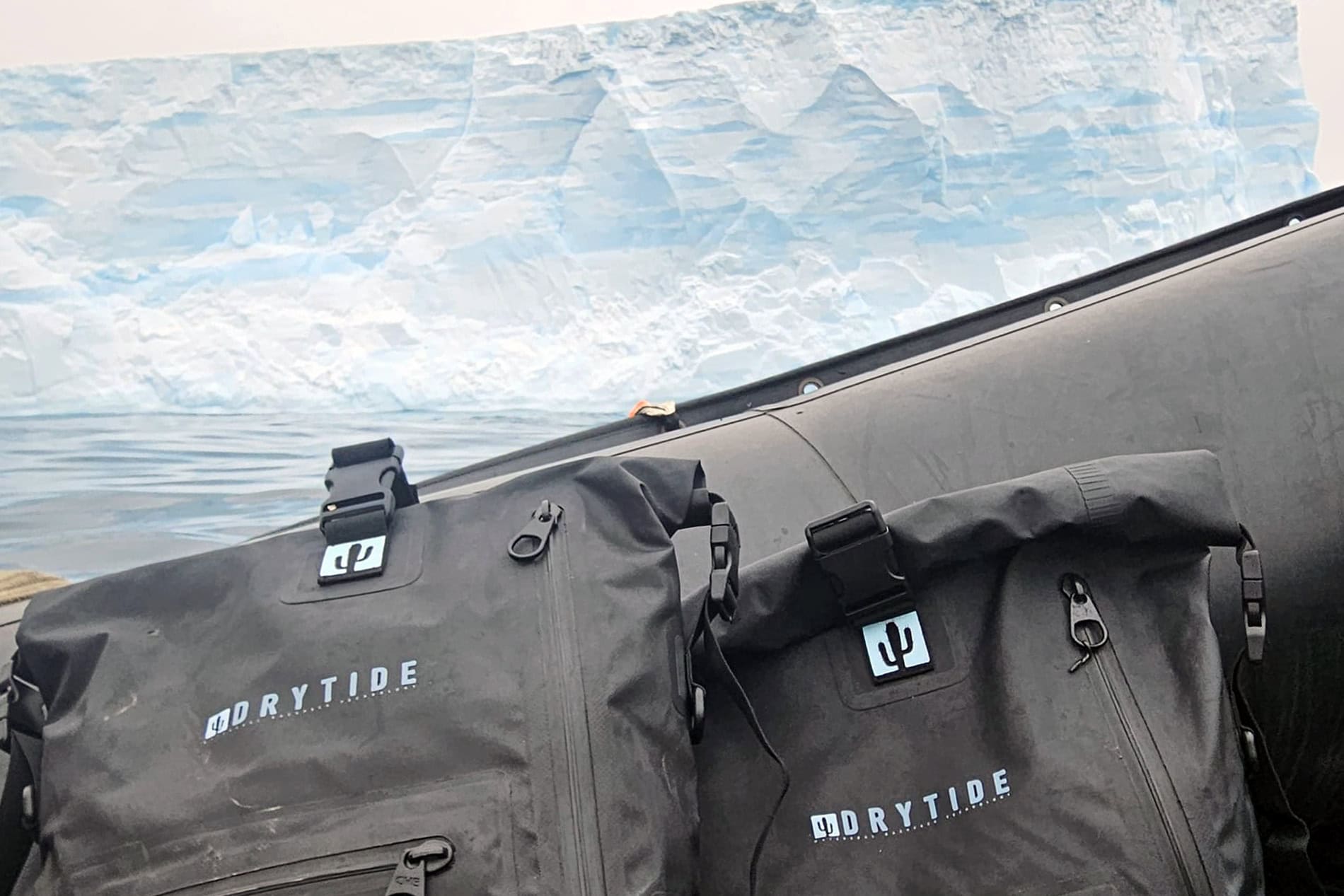Drytide waterproof backpacks and duffels on icy landscape with icebergs.