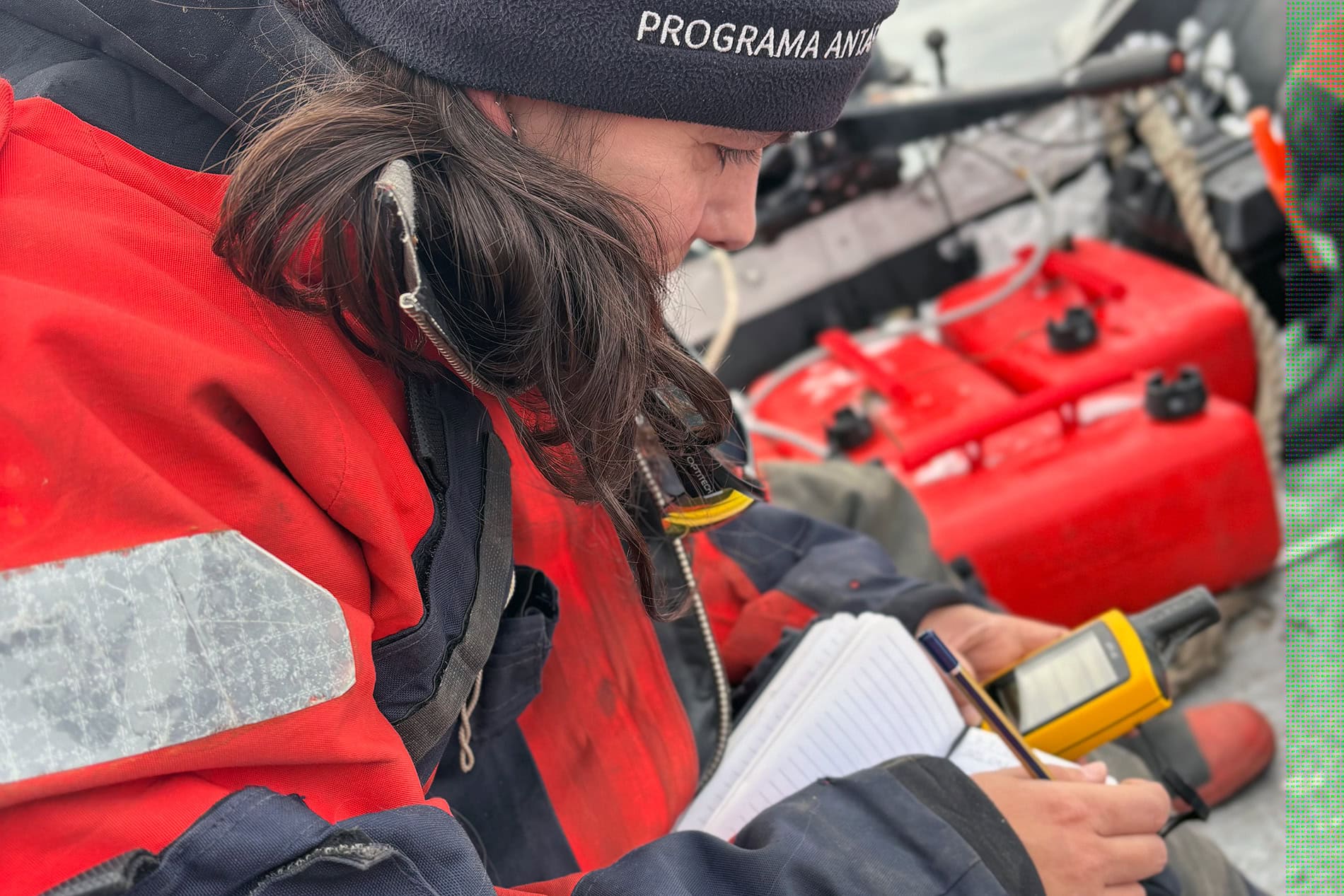 Person in red waterproof gear using a handheld device outdoors.
