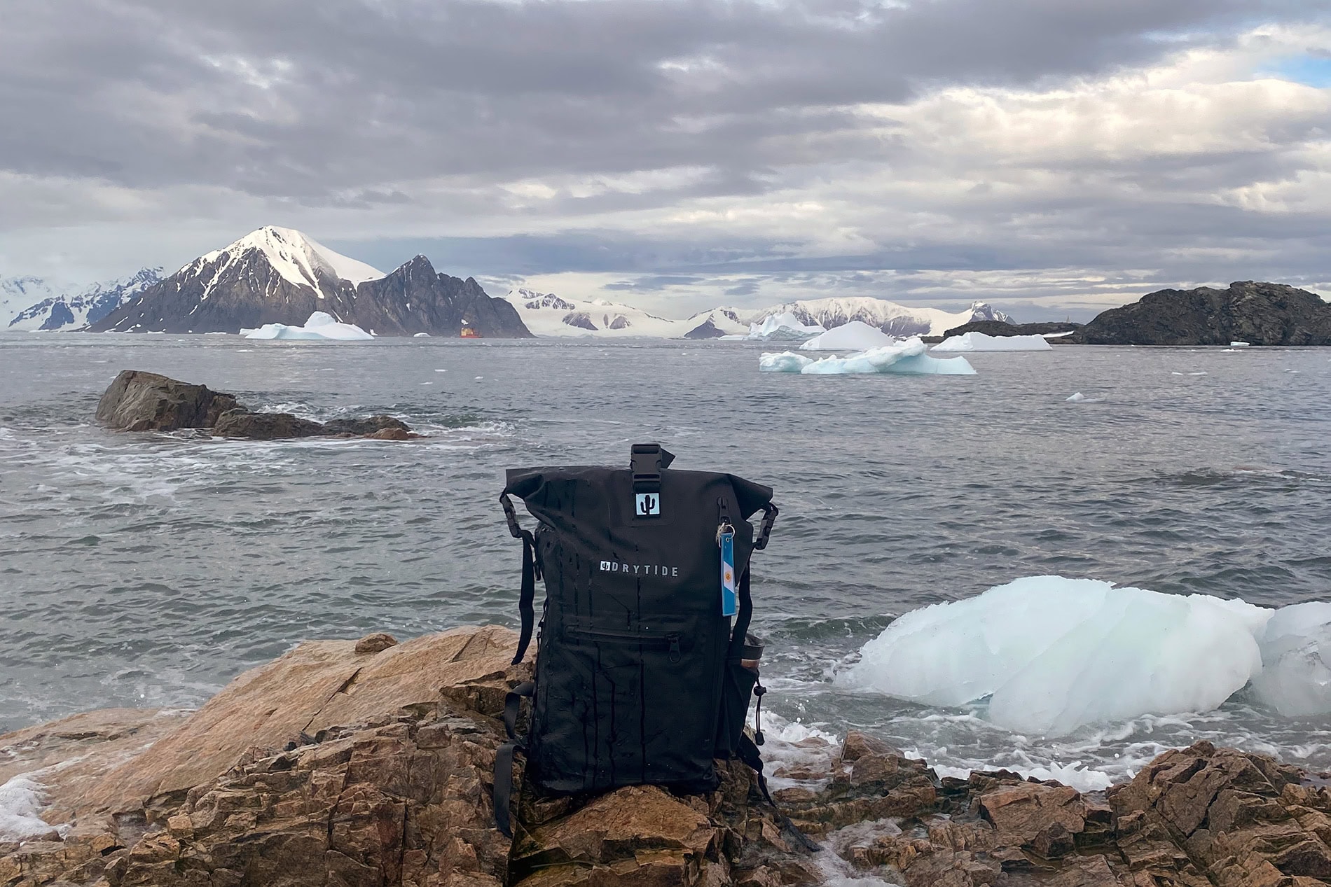 Drytide waterproof backpack on rocky shore with icy landscape in background.