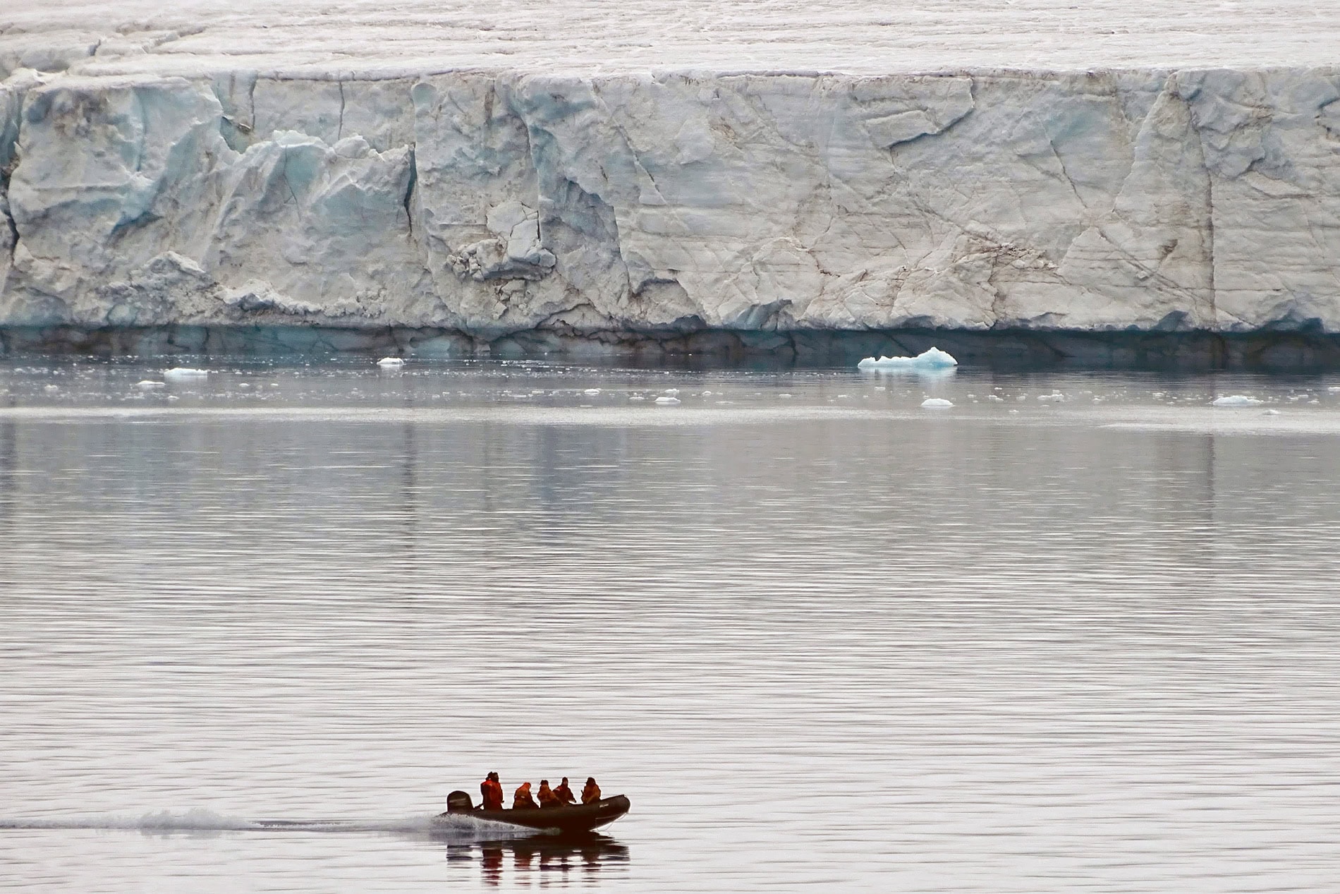 Small boat with people sailing near icy shoreline in cold water.