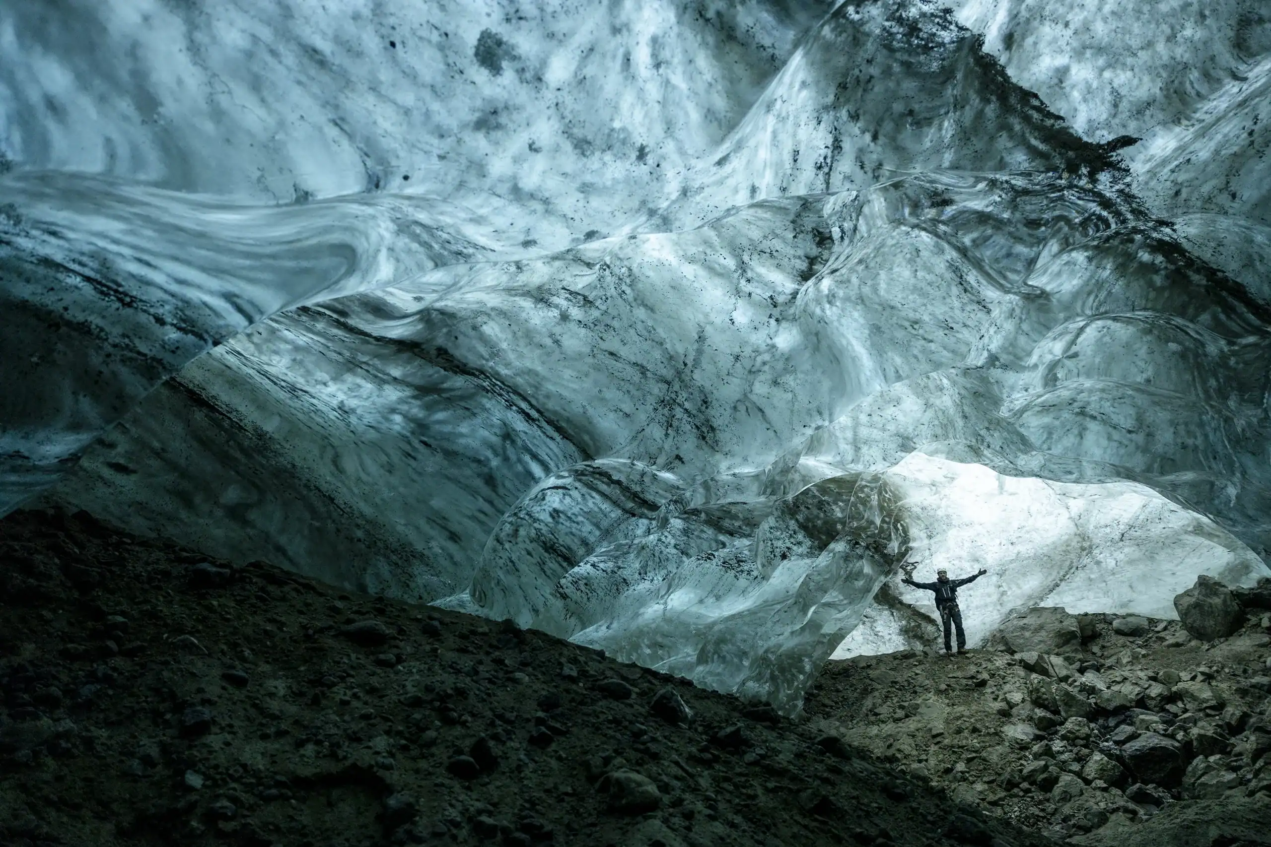 View from inside a subglacial cavern in East Greenland, with an icy ceiling and rocky ground below.