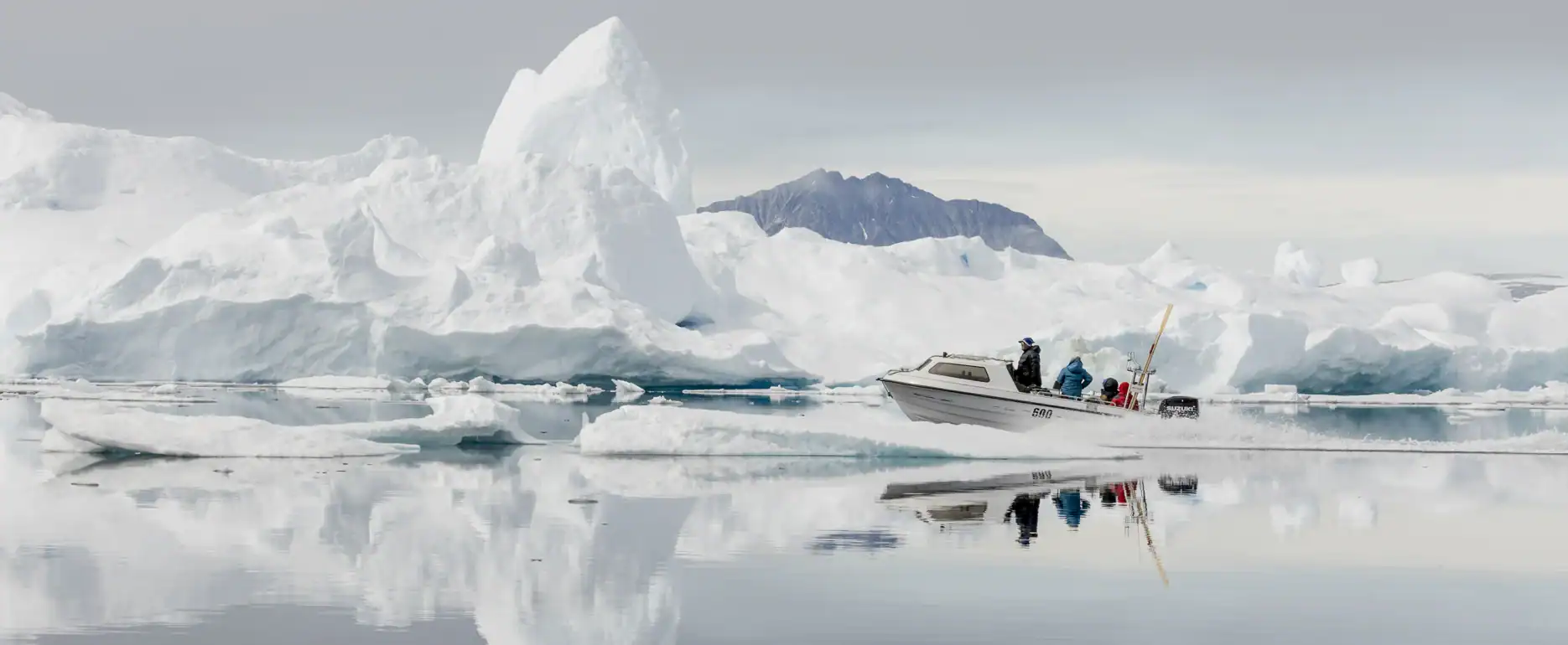 Boat navigating through calm waters surrounded by large icebergs in East Greenland.