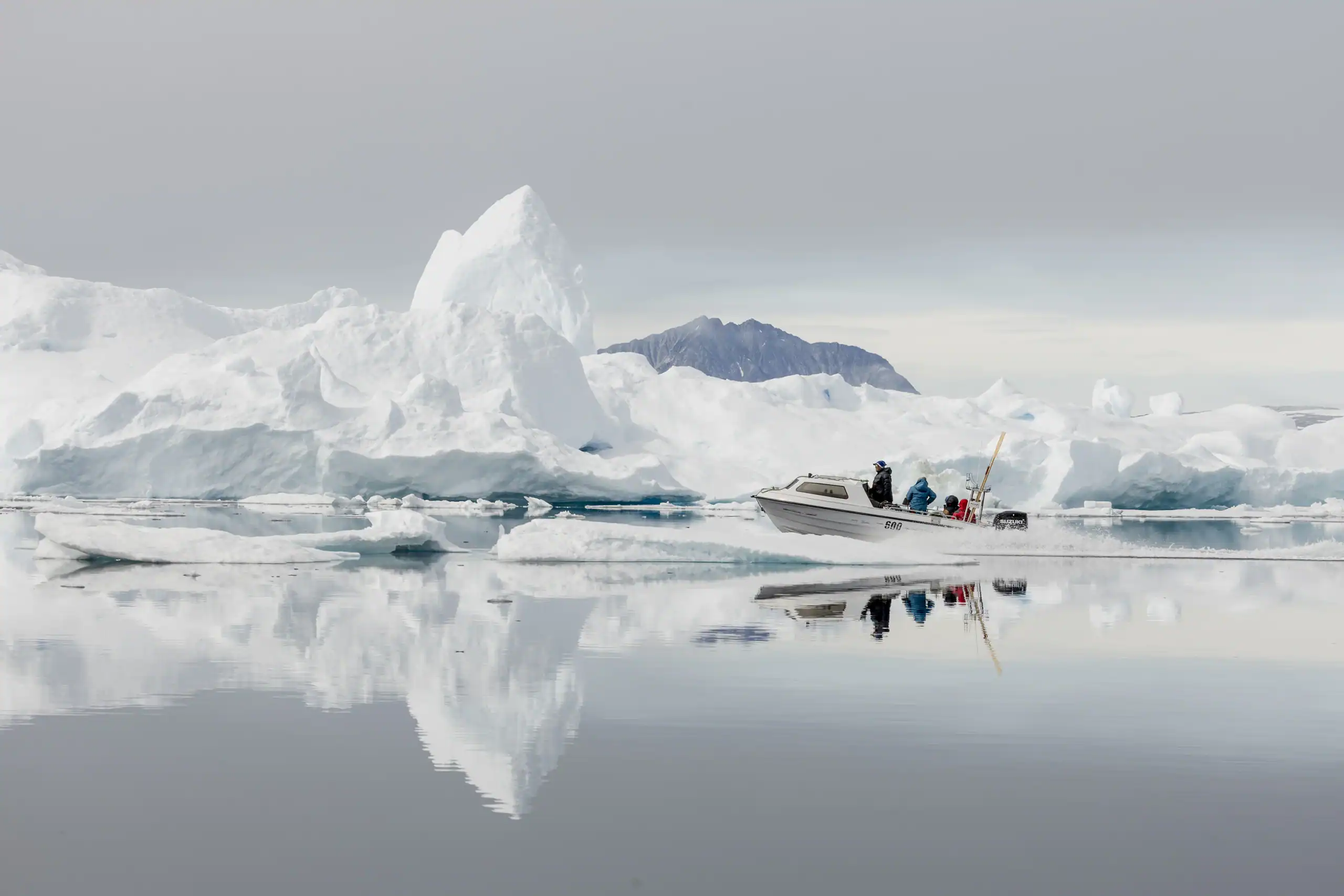 Boat navigating through calm waters surrounded by large icebergs in East Greenland.